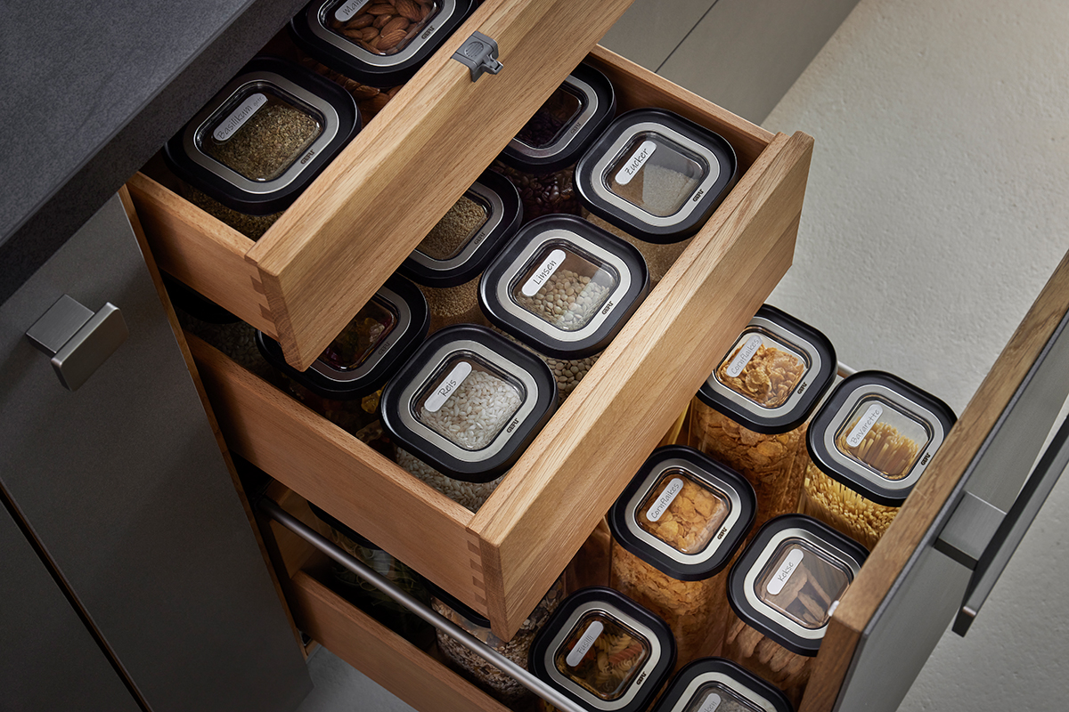 Küchenschubladen-Organisation mit beschrifteten Vorratsbehältern Offene Küchenschubladen gefüllt mit beschrifteten Vorratsbehältern, die Lebensmittel wie Reis, Linsen, Zucker und Mandeln enthalten.