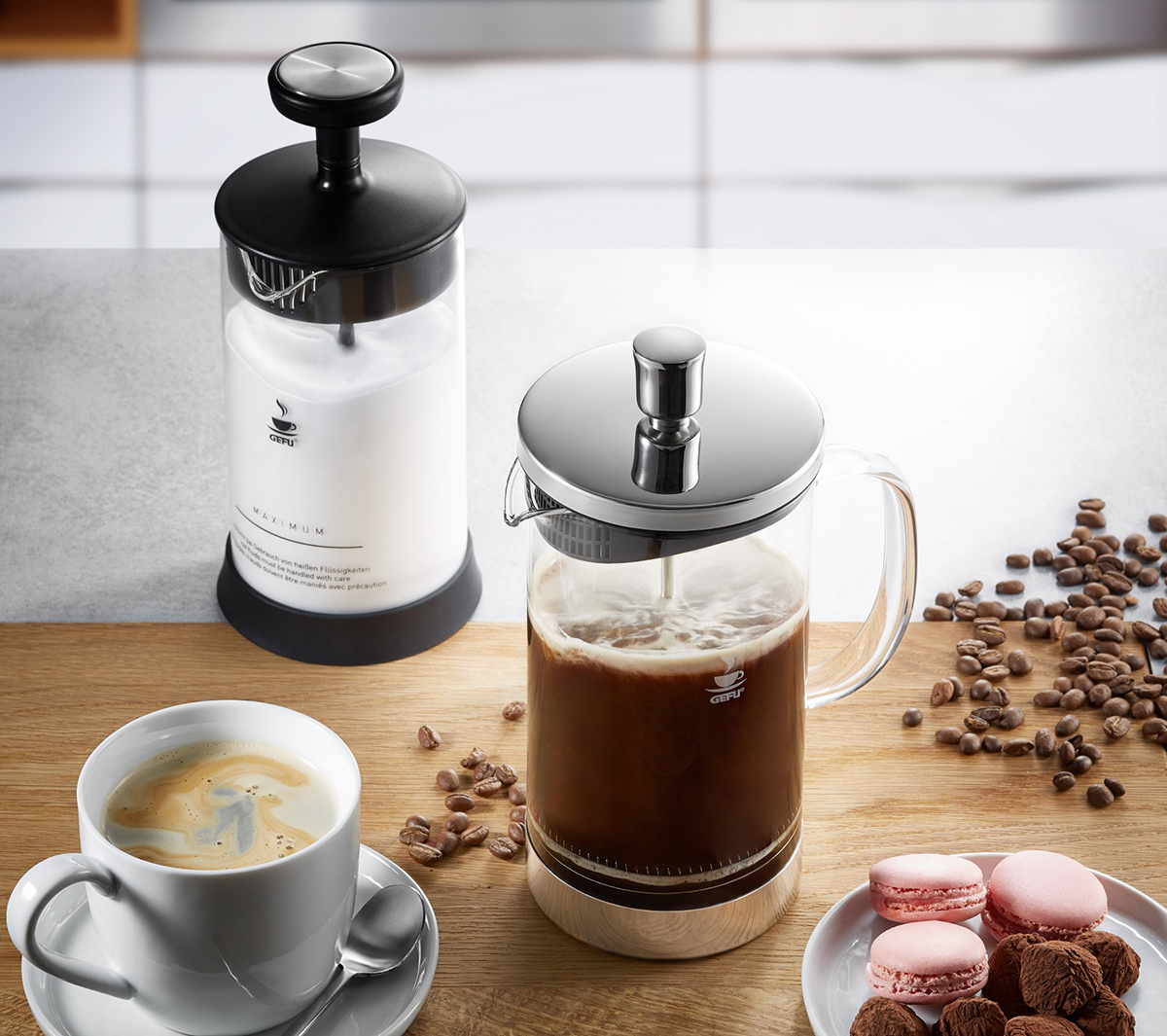 Stilvolle Kaffeeszene mit French Press und Milchschaumspender Ein Coffee-Setup mit French Press, Milchschaumspender, einer Kaffeetasse, Kaffeebohnen und Macarons auf einem Tisch.