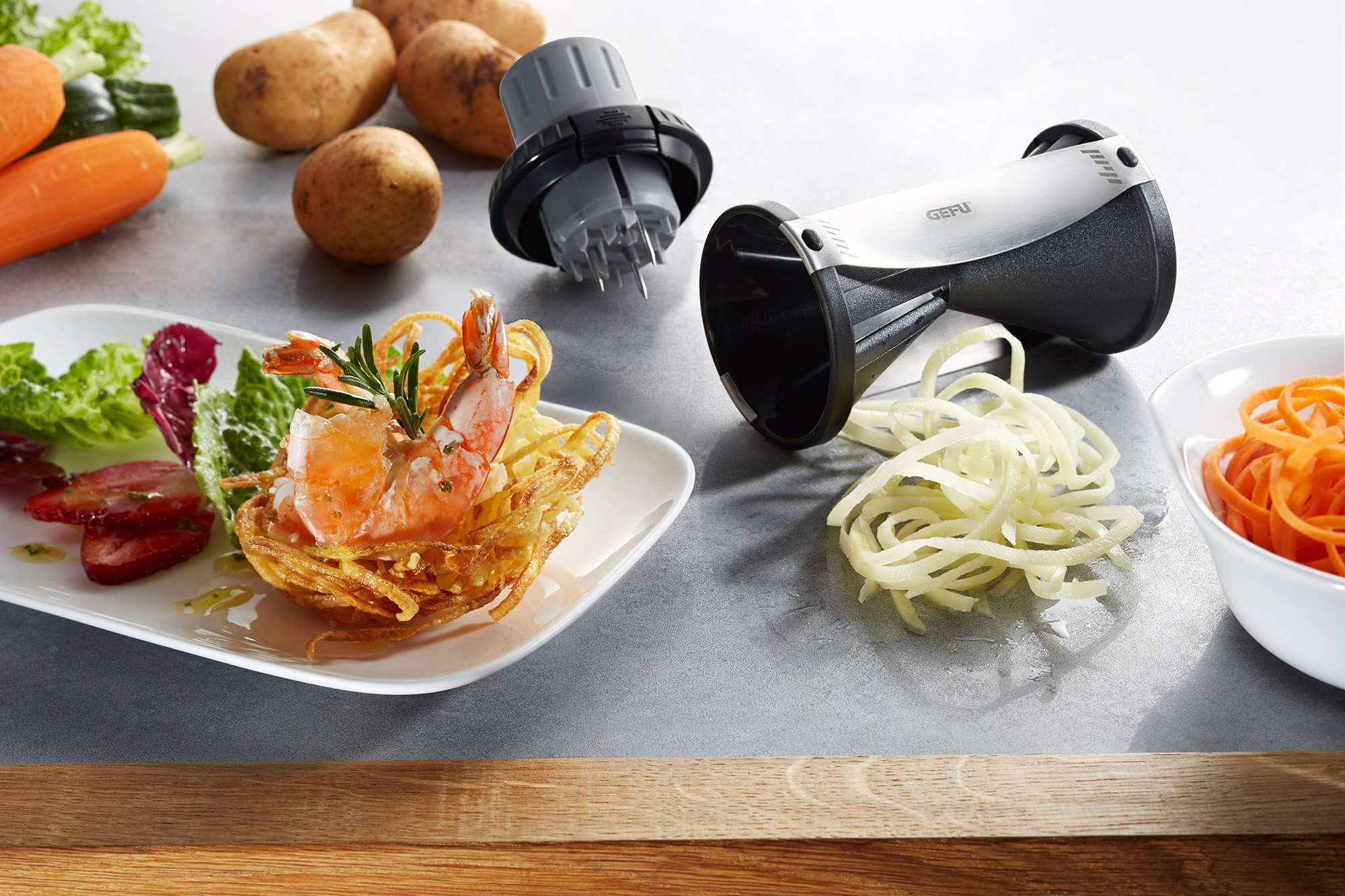 Ein Spiralschneider mit geschnittenen Gemüsenudeln und einem kunstvoll angerichteten Garnelen-Gericht auf einem Teller.