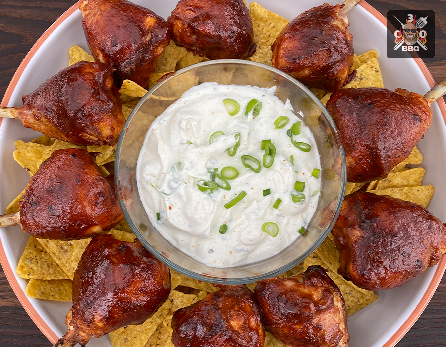 Chicken Lollypops Ein Teller mit BBQ-Hähnchenkeulen, umgeben von Nachos, in der Mitte ein Dip mit Frühlingszwiebeln