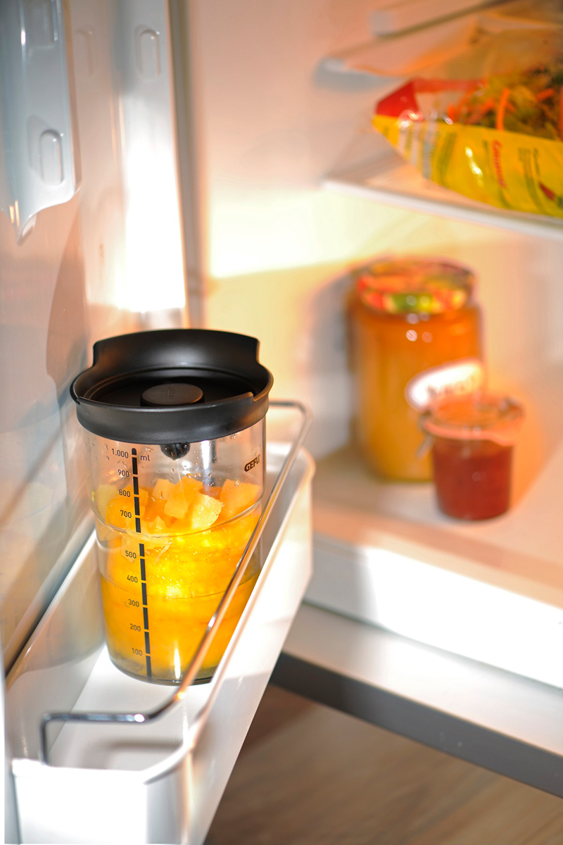 Gefäß mit aufgeschnittenem Obst im Kühlschrank Ein Messbecher mit Deckel, gefüllt mit geschnittenem Obst, steht in der Kühlschranktür. Im Hintergrund sind weitere Gläser zu sehen.