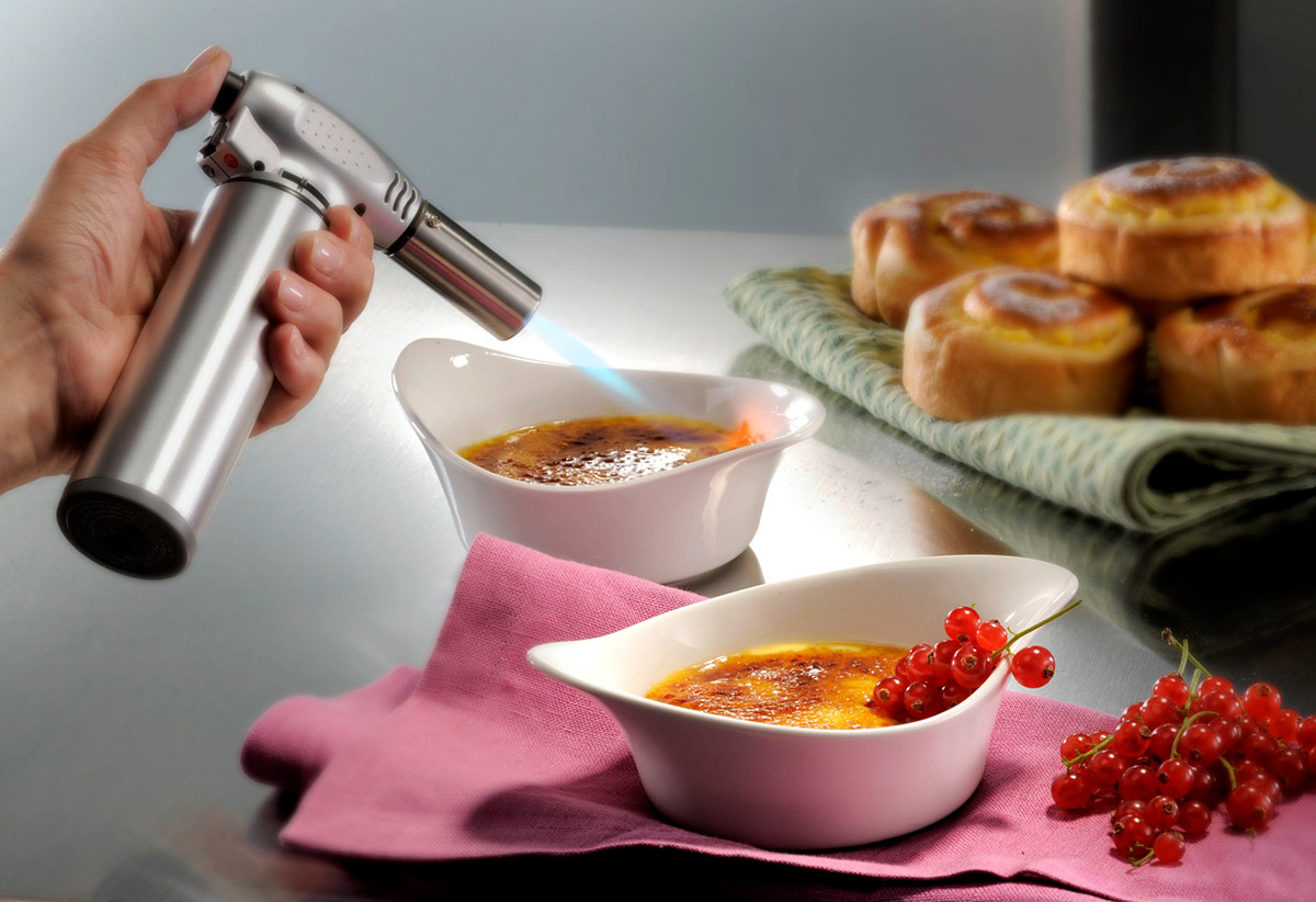 Küchenbrenner für Crème Brûlée - Perfekte Karamellisierung zu Hause Nahaufnahme eines Küchenbrenners, der Crème Brûlée karamellisiert, mit Gebäck im Hintergrund