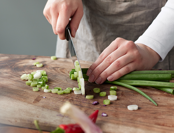 Frische Frühlingszwiebeln auf einem Holzbrett geschnitten Eine Person schneidet mit einem Messer Frühlingszwiebeln auf einem Holzbrett in der Küche