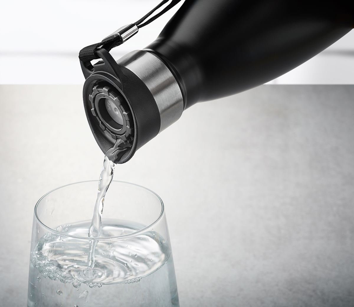Nahaufnahme einer schwarzen Thermosflasche, die Wasser in ein klares Glas gießt, auf grauem Hintergrund