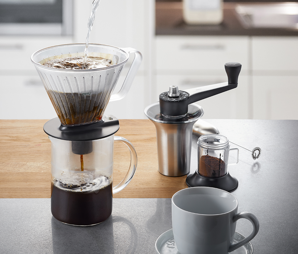 Kaffeefilter-Set mit Handmühle und Tasse in moderner Küche Kaffeefilter aus Glas beim Aufbrühen, daneben Handkaffeemühle und leere Tasse auf Küchenarbeitsfläche