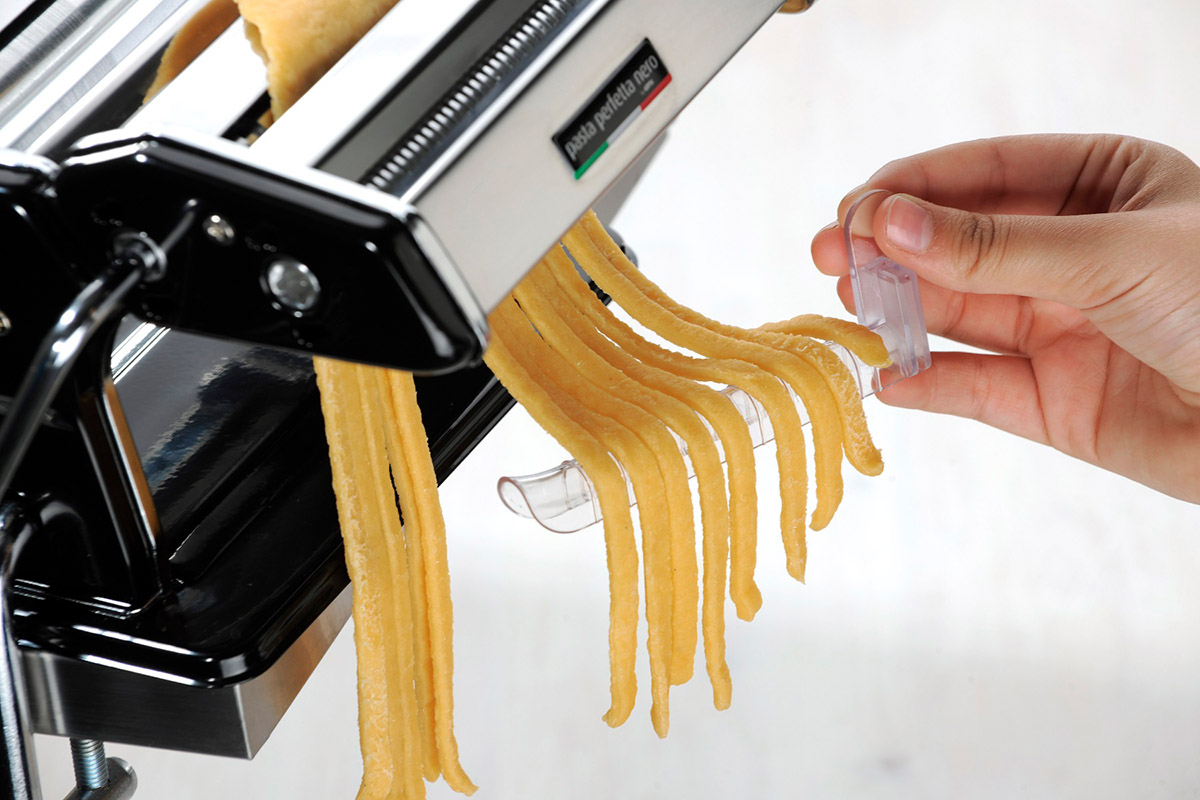 Nudelmaschine mit frischer Pasta Hand, die Nudeln aus einer Nudelmaschine zieht