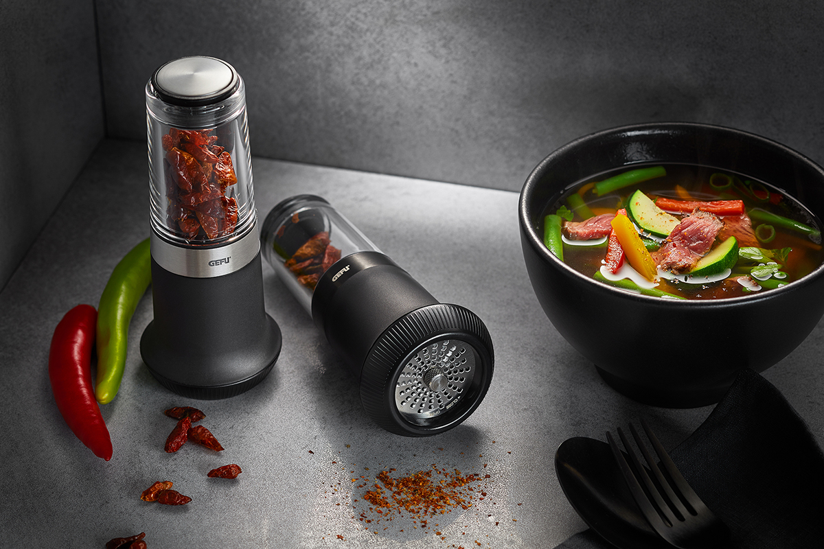 Elektrische Chilimühle und frische Suppe in einer modernen Küchenszene mit roten und grünen Chilis