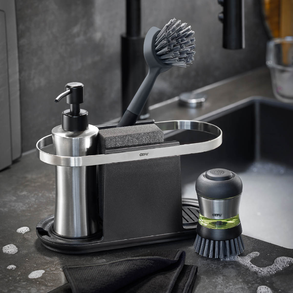 Hochwertiges Spülset mit Seifenspender, Bürste und Schwammhalter Spülset auf einer Küchentheke mit Seifenspender, Spülbürste und Schwammhalter von GEFU, ideal für eine organisierte Küchenreinigung
