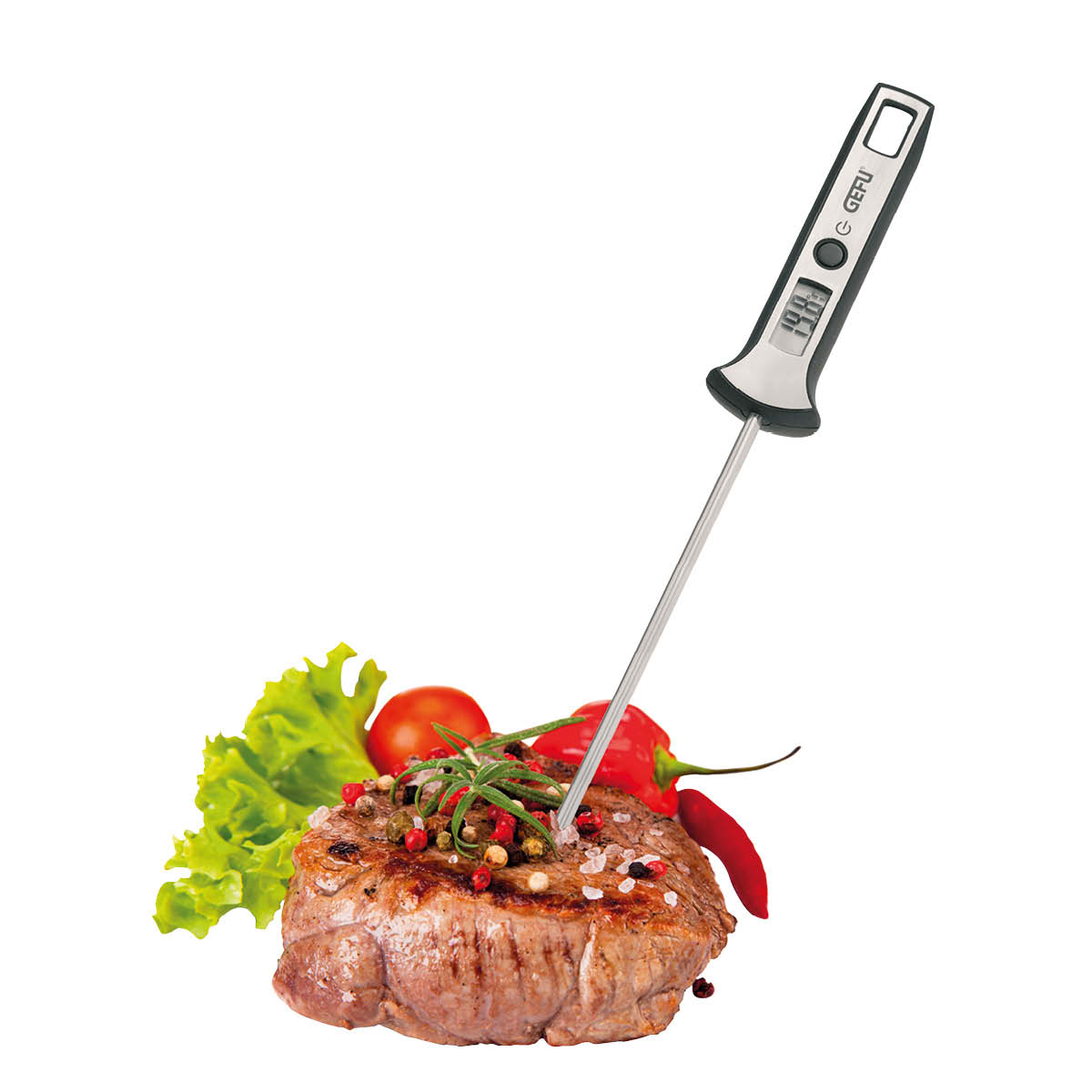 Fleischthermometer mit Steak und Gemüse Ein digitales Fleischthermometer misst die Temperatur eines Steaks, das mit Kräutern und Gewürzen garniert ist. Im Hintergrund sind Tomaten und Salat zu sehen.