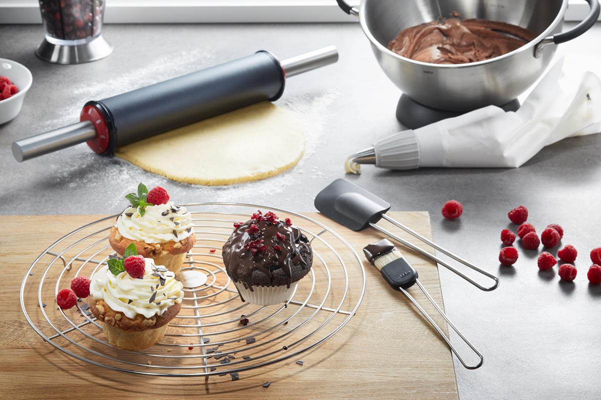 Backzubehör-Set mit Nudelholz, Teigschüssel, Spritzbeutel und dekorierten Muffins auf einem Tisch