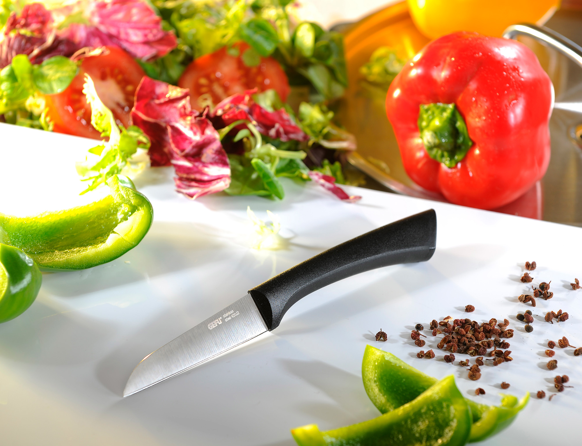Küchenmesser mit schwarzem Griff neben frischem Gemüse auf Schneidebrett Schwarzes Küchenmesser liegt auf einem Schneidebrett neben grünem und rotem Paprika, Tomaten und Salatblättern