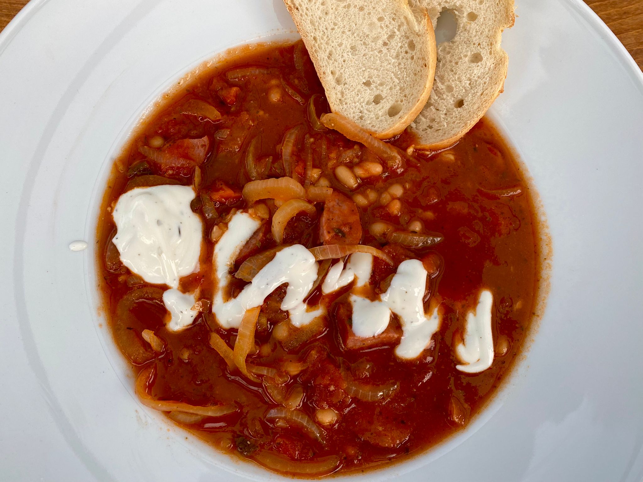 KABANOSSI Zwiebelsuppe Nahaufnahme einer deftigen Gemüsesuppe mit einer Scheibe Weißbrot und einem Klecks Sahne auf einem weißen Teller