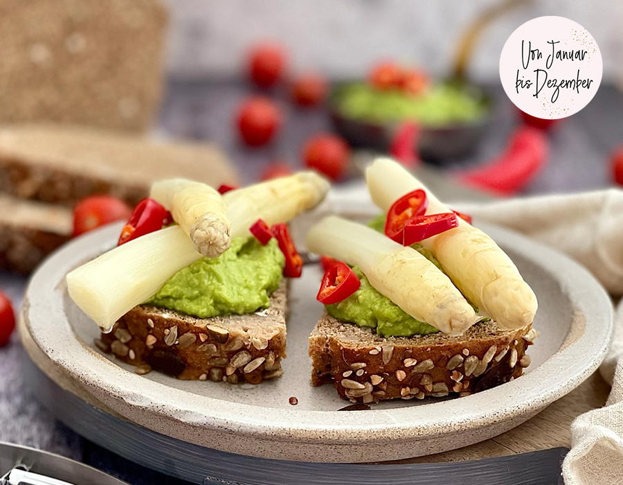 Körnerbrot mit Avocadocreme und Spargel Zwei Scheiben Vollkornbrot mit Avocadocreme, weißem Spargel und roten Chilischoten auf einem Teller