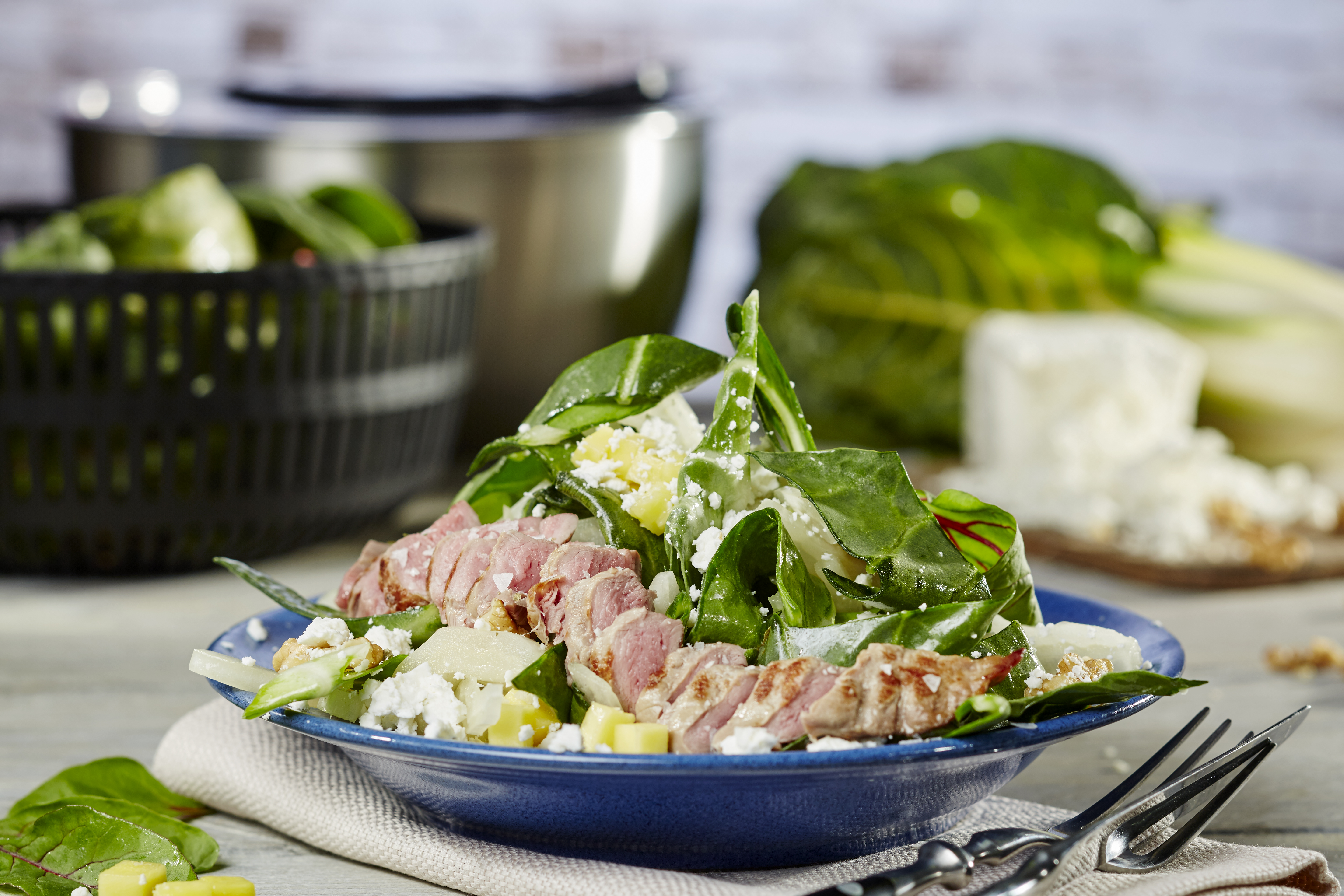 Mangoldsalat mit Walnüssen und gebratenen Lammfilets  Ein Teller mit frischem Spinatsalat, gegrilltem Fleisch und Feta, serviert auf einem blauen Teller