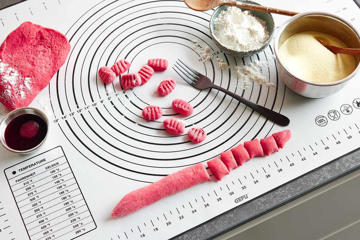 Rote Gnocchi-Zubereitung auf einer Antihaft-backmatte mit Gabel und Mehl Rote Gnocchi-Knödel in Vorbereitung auf einer Antihaft-backmatte, umrundet von einem Teig, Mehl, Wein und einer Gabel