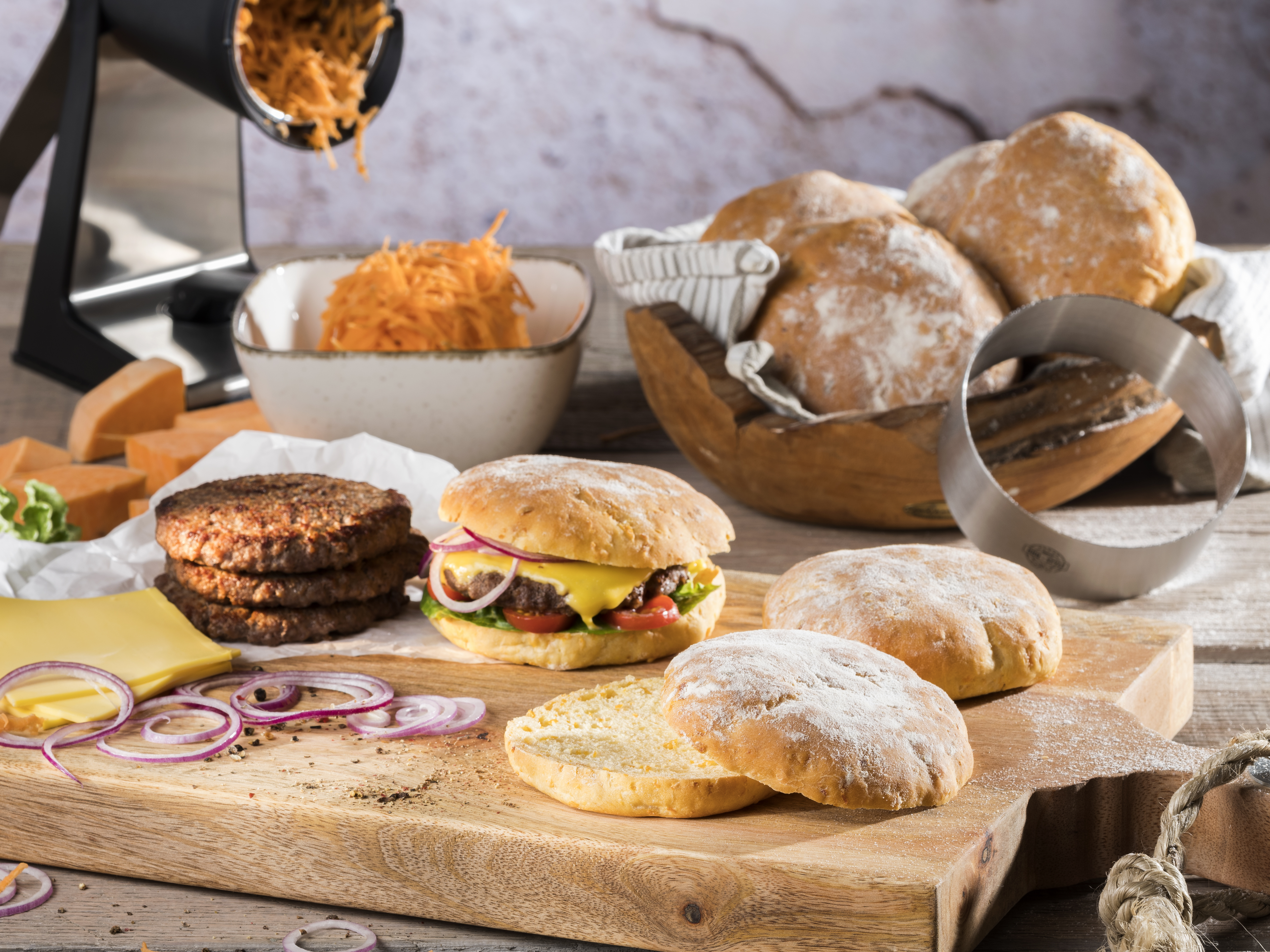 Süßkartoffel-Burger-Buns Verschiedene Zutaten für Hamburger, darunter Weizenbrötchen, Burger-Patties, Käsescheiben, Tomaten und Zwiebeln, auf einem Holzbrett arrangiert.
