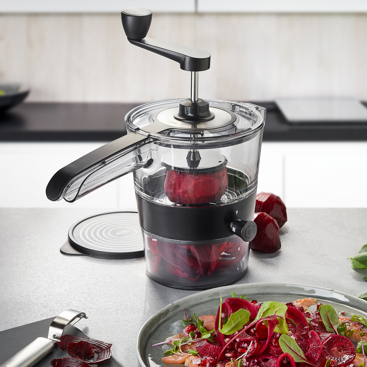 Manuelle Gemüseschneider für frische Salate und kulinarische Kreationen Ein manueller Gemüseschneider auf einer Küchenarbeitsplatte neben einem Teller mit frischem Salat