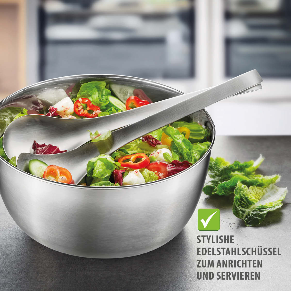 Moderne Edelstahlschüssel mit Salatbesteck zum Anrichten Edelstahlschüssel mit frischem Salat und Besteck auf einem Tisch, perfekt zum Servieren geeignet