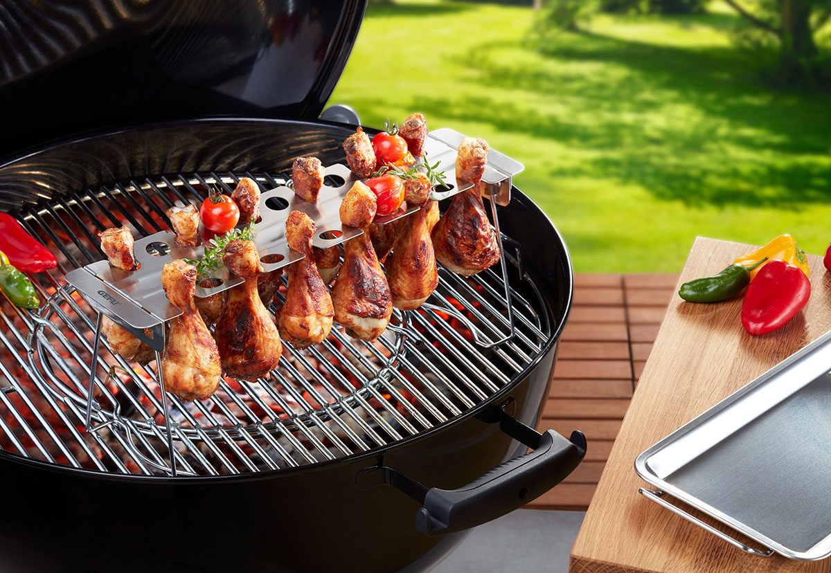 Leckere Hähnchenschenkel auf einem Grill mit Gemüse im Freien zubereitet Nahaufnahme von gegrillten Hähnchenschenkeln auf einem Grill, garniert mit Kirschtomaten und Kräutern, in einem Garten.