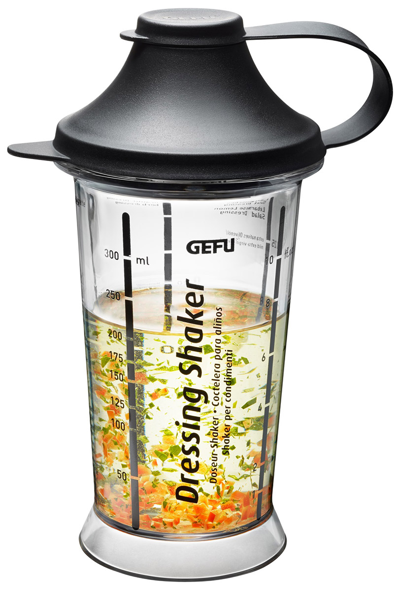 Ein transparenter Dressing Shaker der Marke GEFU mit Messskala und schwarzem Deckel, gefüllt mit Kräutermischung und Flüssigkeit.