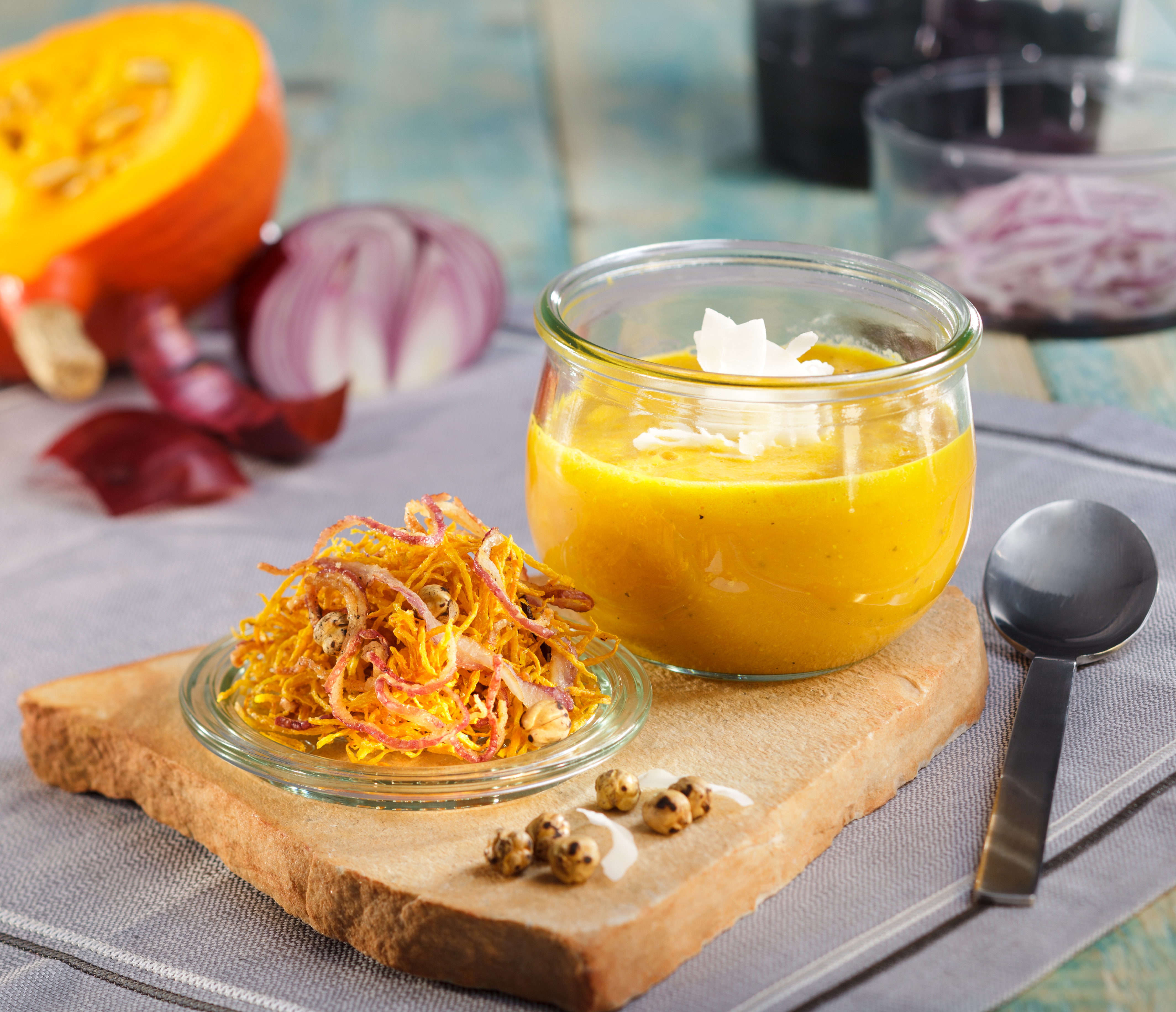 Kürbiscremesuppe mit Kürbis-Zwiebel-Stroh Frische Kürbissuppe im Glas serviert auf einem Holzbrett mit knusprigen Zwiebelringen als Beilage