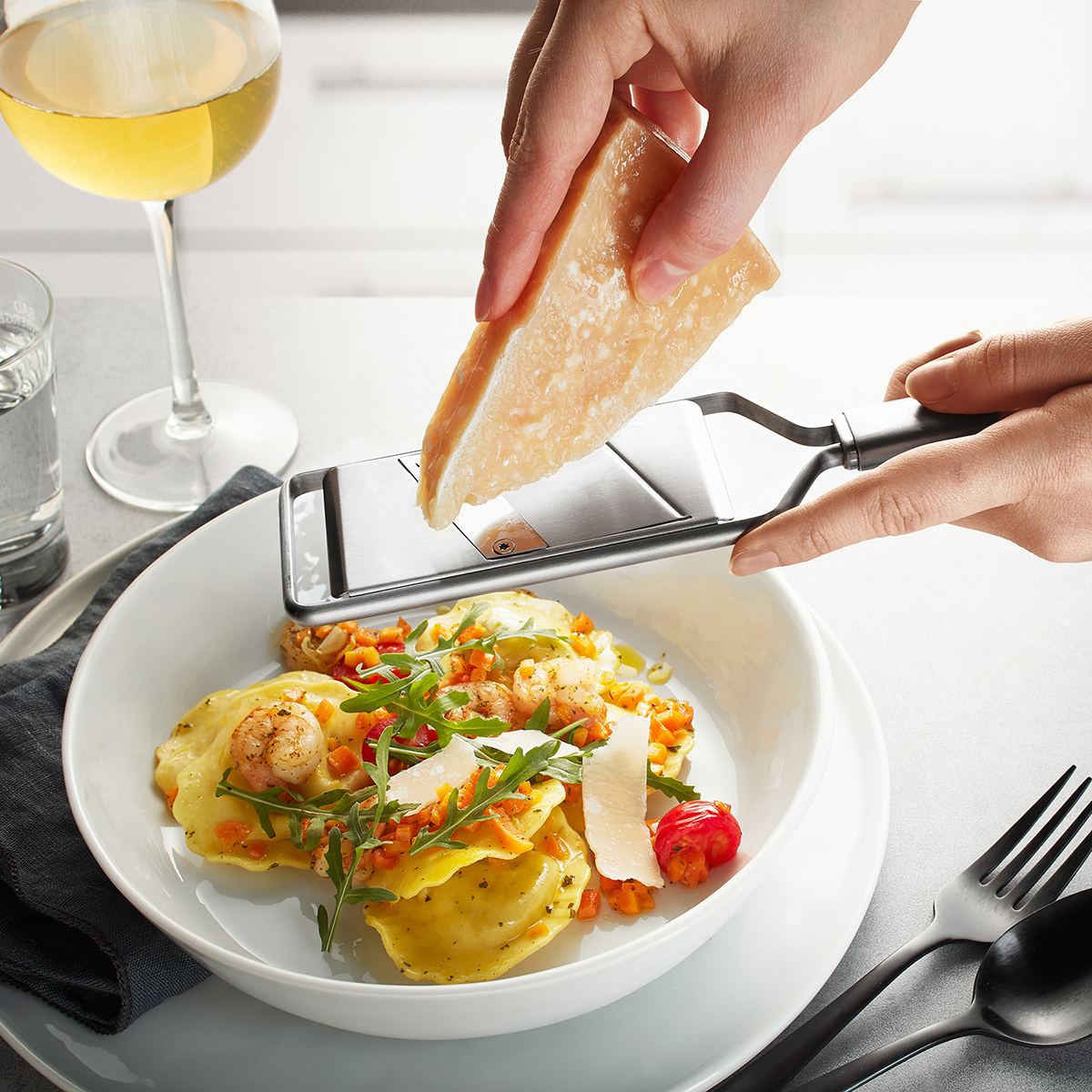 Frisch geriebener Parmesan über Ravioli mit Rucola und Garnelen Nahaufnahme einer Hand, die Parmesan über ein Gericht mit Ravioli, Garnelen und Rucola reibt