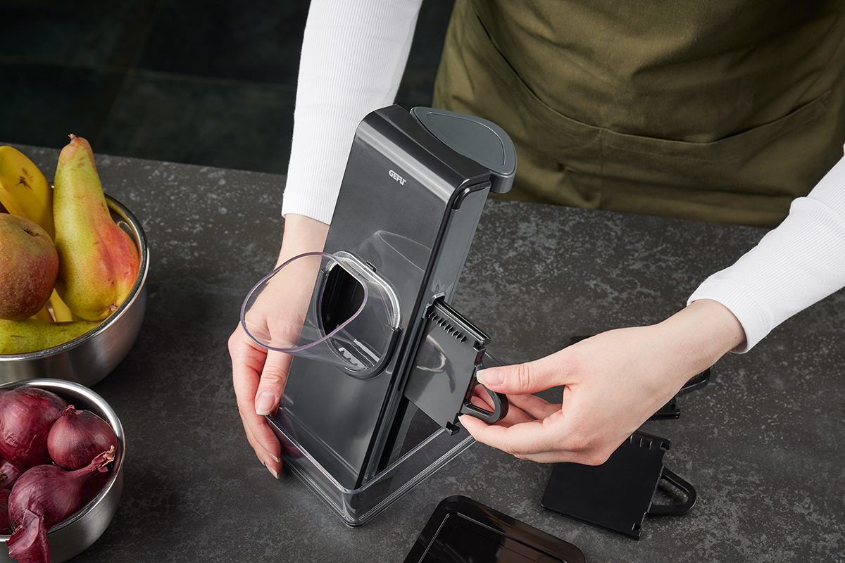 Hochwertige Gemüsehobelmaschine in der Anwendung Person justiert einen Gemüsehobel neben einer Schale mit Obst und Gemüse.