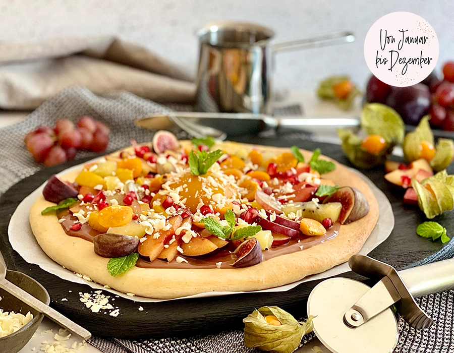 Süße Pizza Frische Fruchtpizza, dekoriert mit verschiedenen Früchten, Minze und geriebenem Käse, auf schwarzem Servierteller.