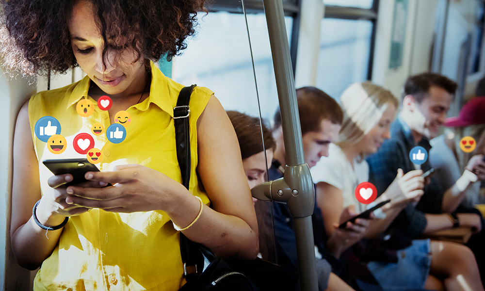 Personen nutzen Smartphones in der U-Bahn mit Social-Media-Interaktionen Mehrere Menschen in einer U-Bahn, die auf ihren Smartphones Social-Media-Apps nutzen, mit Emojis über den Bildschirmen.