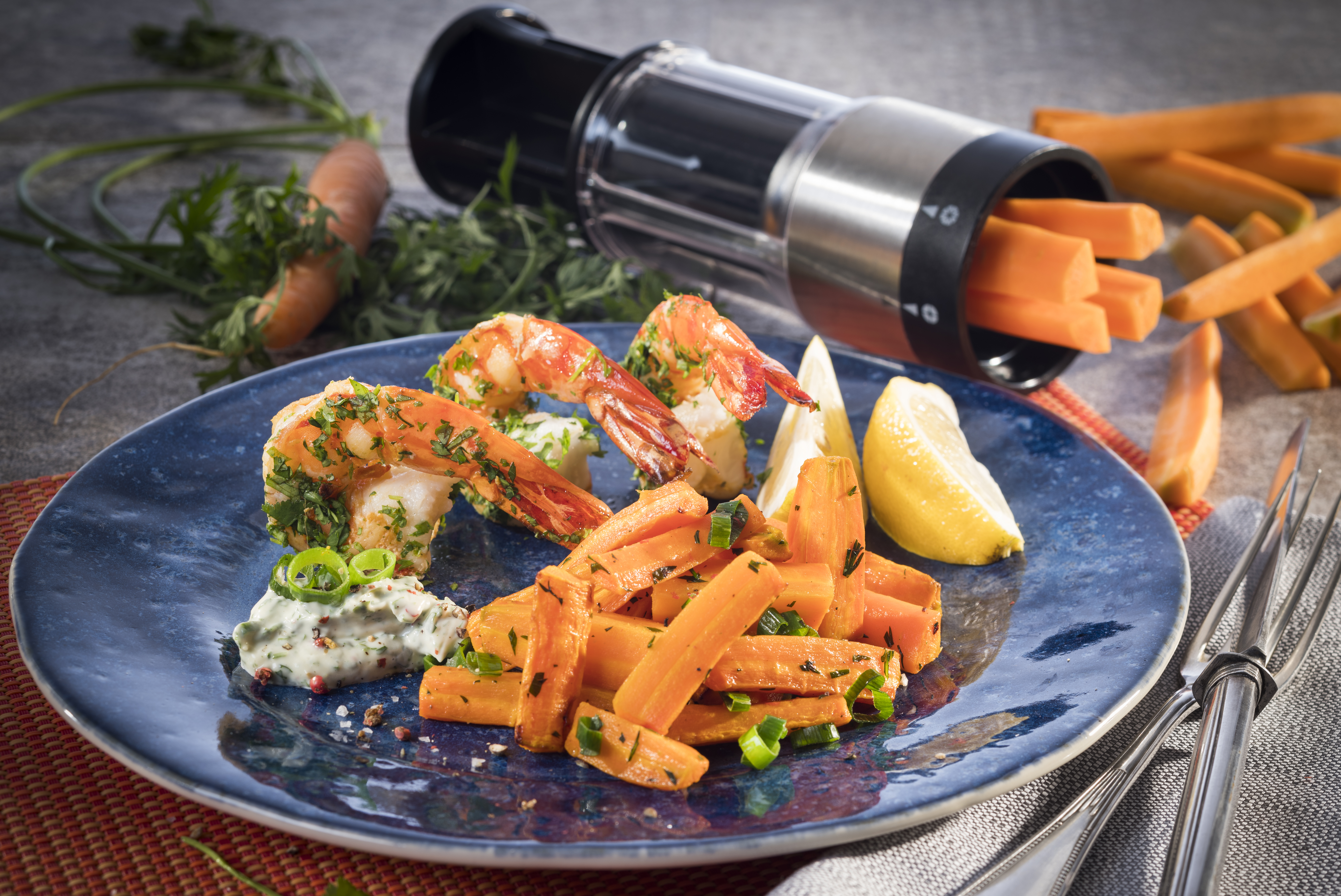 Gebackene Möhren-Sticks mit gebratener Riesengarnele und Knoblauch-Kräuter-Mayonnaise Gericht aus Garnelen und Karottensticks auf blauem Teller, garniert mit Kräutern und Zitronenscheibe