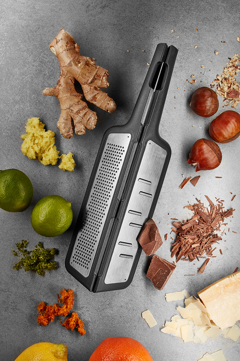 Multifunktionale Küchenreibe mit Ingwer, Limetten, Schokolade und Käse Küchenreibe umgeben von frischen Zutaten wie Ingwer, Limetten, Schokolade und Käse