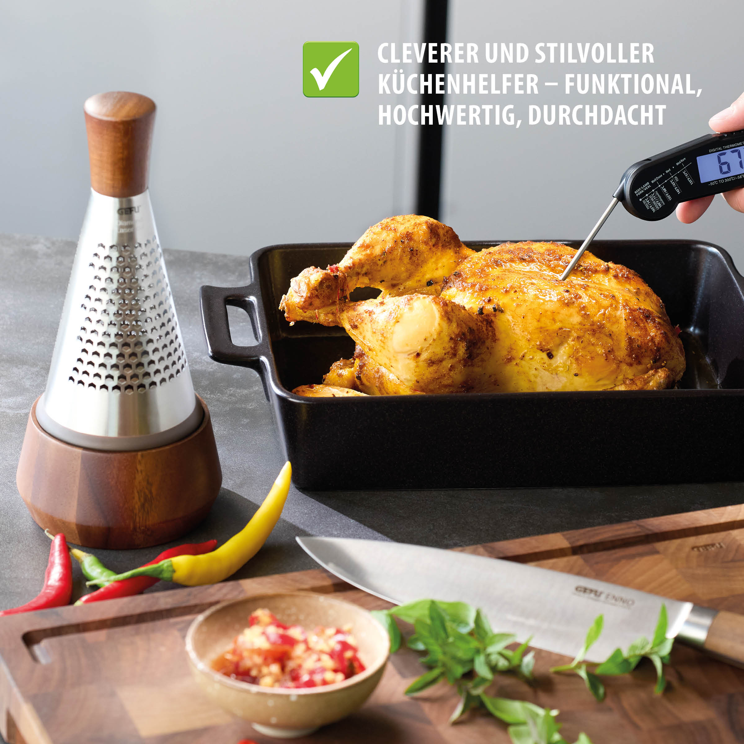 Kegelreibe CASEO von GEFU aus Edelstahl mit Schale und Löffel in Walnussholzoptik auf einer Arbeitsplatte neben gebratenem Hähnchen, Messer und frischen Zutaten, ideal zum Reiben von Käse, Schokolade und Gewürzen