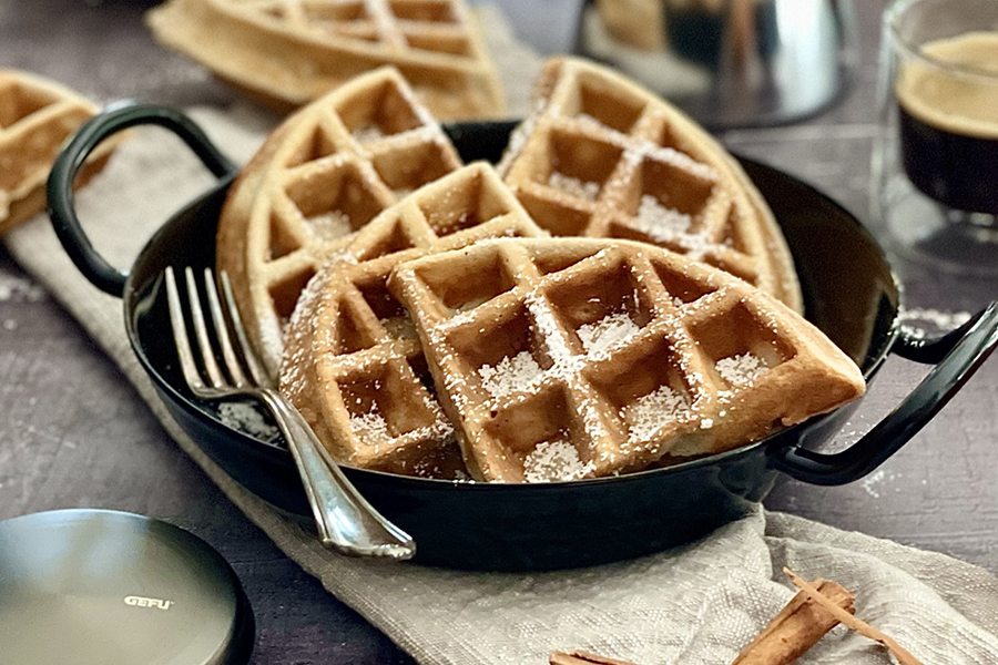 Apfel-Zimt-Waffeln Belgische Waffeln mit Puderzucker in schwarzer Pfanne mit Gabel und Tasse Kaffee