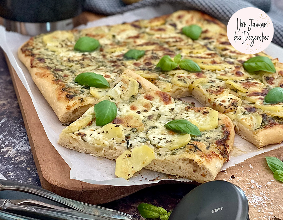 Kartoffelpizza mit Basilikum-Pesto Frisch gebackener Flammkuchen mit Kartoffelscheiben und Basilikumblättern, serviert auf einem Holzbrett