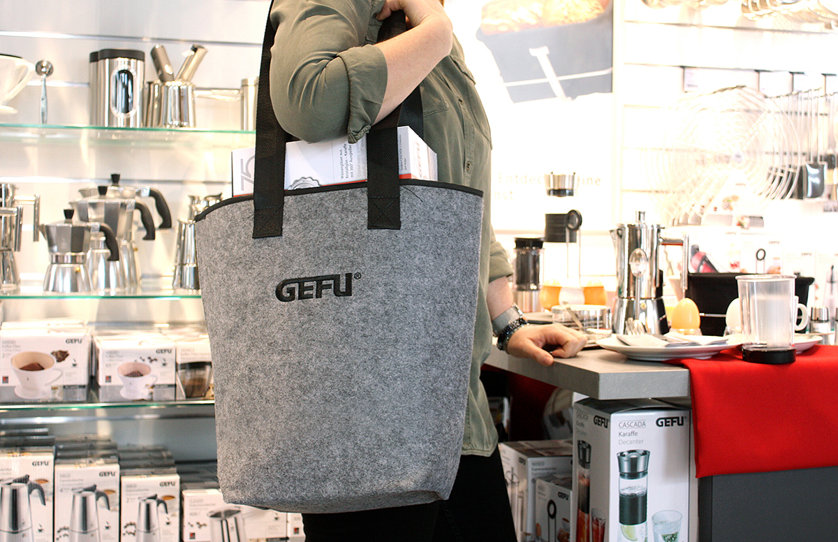 Person mit GEFU Filztasche in einem Küchenfachgeschäft umgeben von Küchengeräten und Geschirr