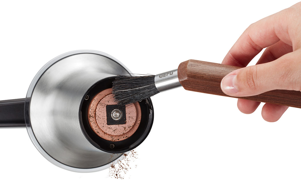 Kaffeebohnenmühle mit Reinigungsbürste Nahaufnahme einer Kaffeemühle, die mit einer speziellen Reinigungsbürste gesäubert wird, um Kaffeereste zu entfernen.
