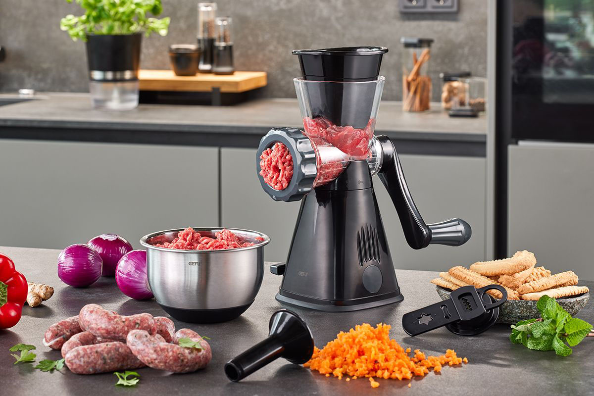 Manuelle Fleischwolf-Maschine auf einer modernen Küchenarbeitsplatte Fleischwolf auf einer Küchenarbeitsplatte mit Fleisch, Karotten und Keksen