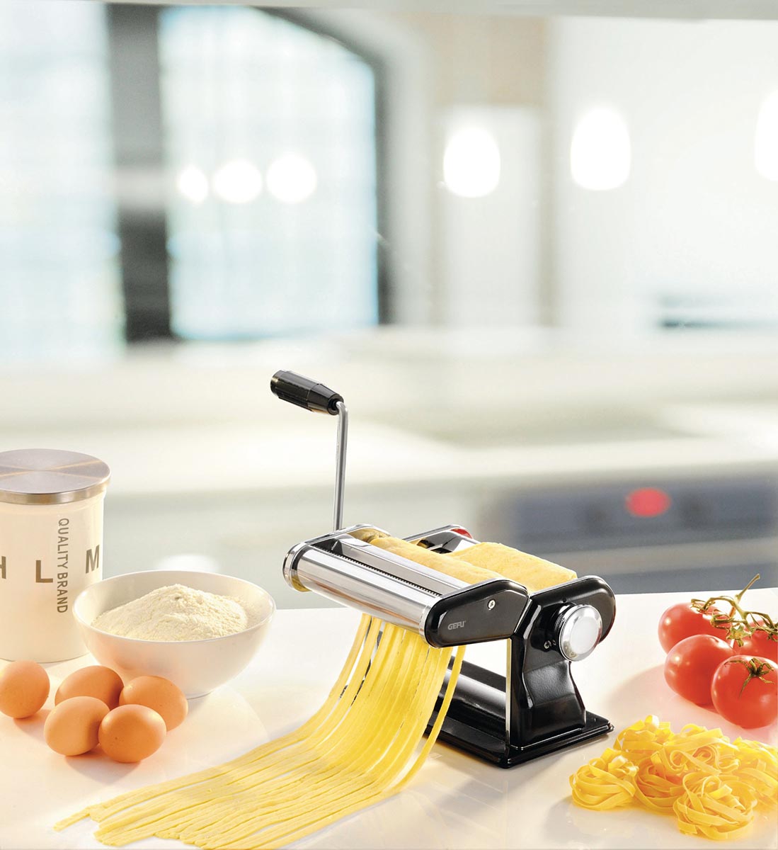 Manuelle Nudelmaschine für frische hausgemachte Pasta Manuelle Nudelmaschine neben frischen Zutaten wie Mehl, Eiern und Tomaten in einer modernen Küche