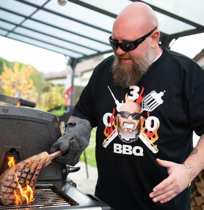 Mann mit Grill trägt humorvolles BBQ-T-Shirt Mann grillt Fleisch und trägt ein lustiges BBQ-T-Shirt
