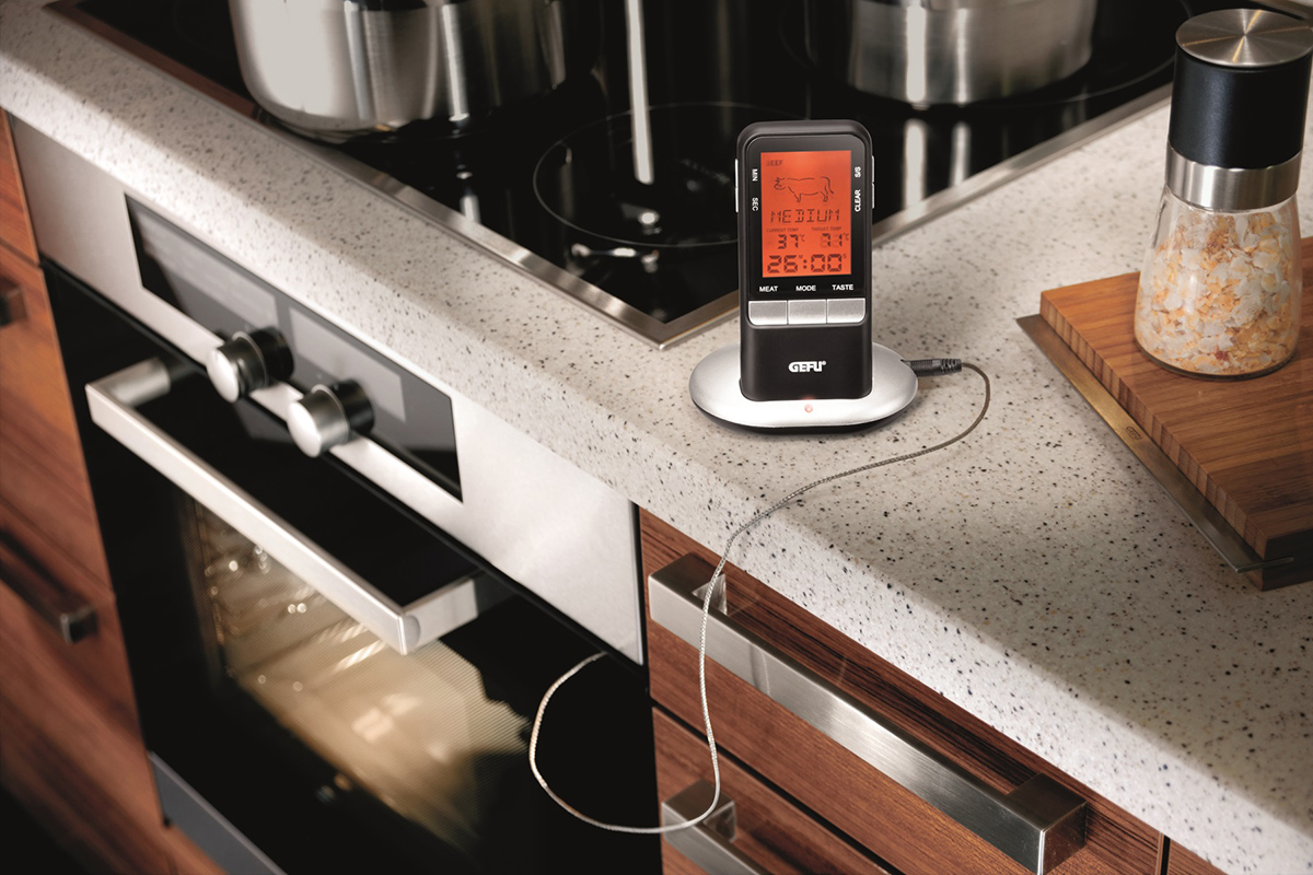 Digitales Küchenthermometer mit Timer auf einer modernen Küchenarbeitsfläche Ein digitales Küchenthermometer mit Timer-Funktion steht auf einer Küchenarbeitsfläche neben einem Gewürzbehälter und einem modernen Ofen