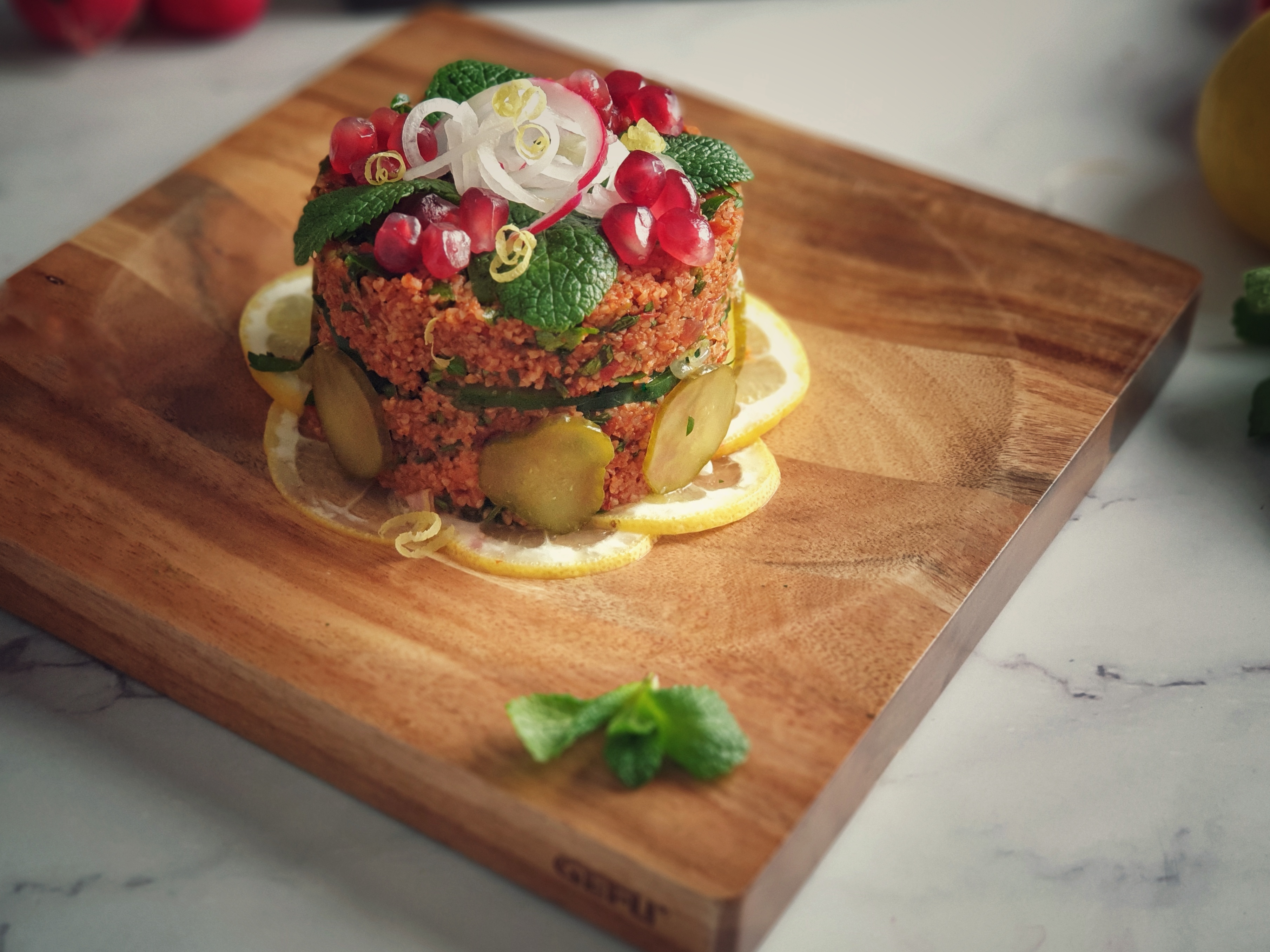 Bulgur-Salat Ansprechend präsentierter Couscous-Salat mit Granatapfel, Gurken und Minze auf einem Holzbrett