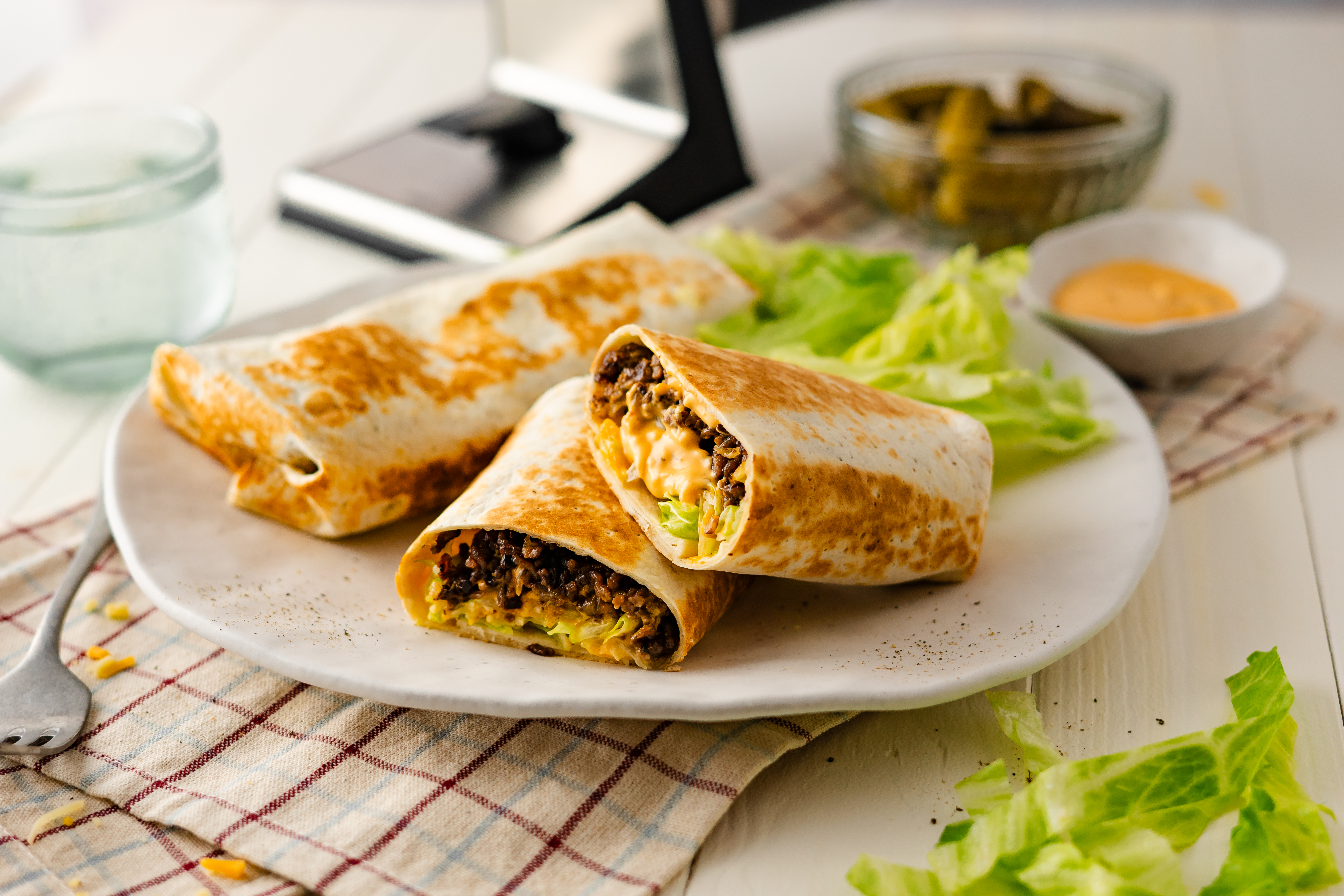 Hamburger Wraps mit selbst gemachtem Hackfleisch Nahaufnahme von gefüllten Wraps, angerichtet mit Salat und einer Schale Sauce im Hintergrund, auf einem Teller serviert