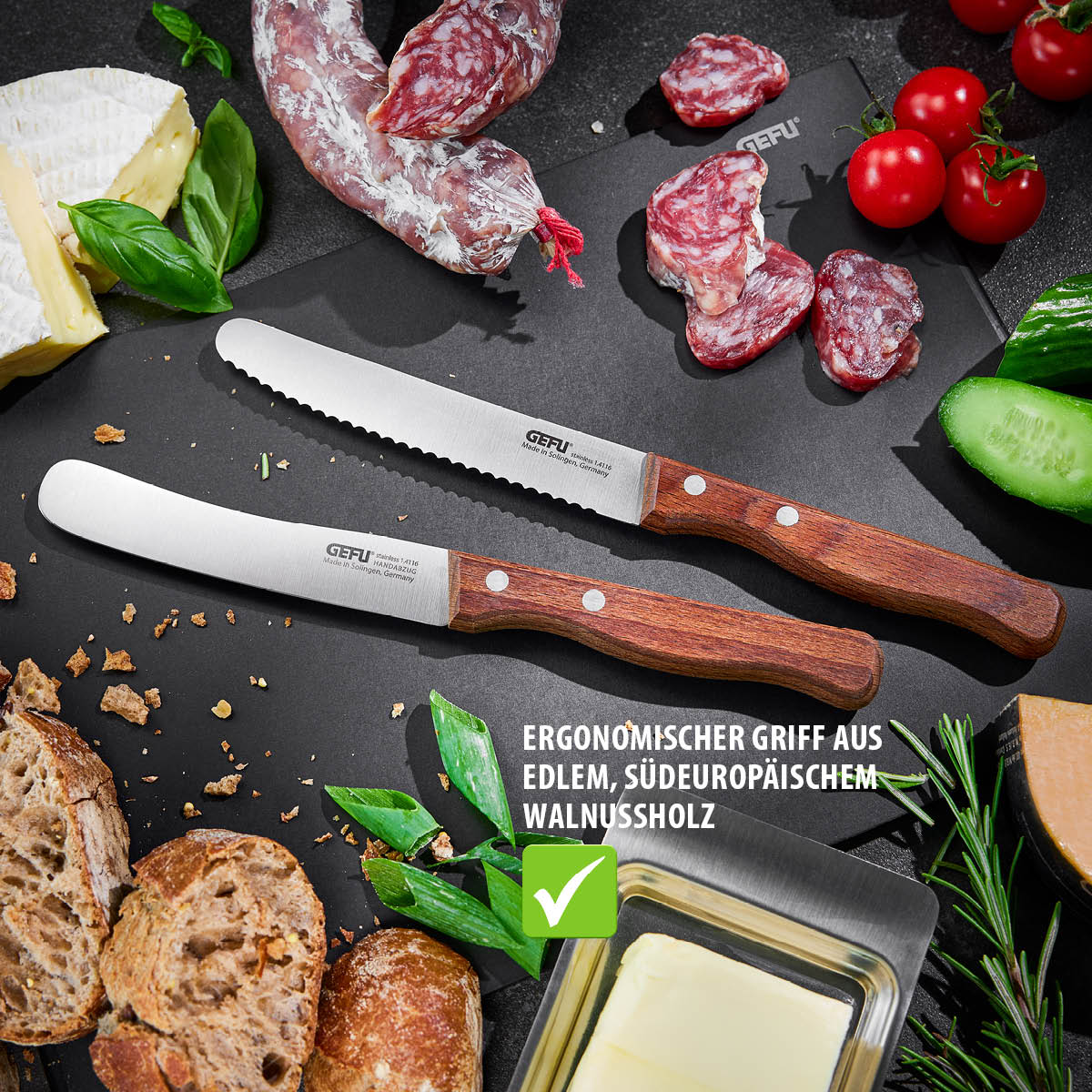 Zwei Tafelmesser mit Holzgriff, umgeben von Brot, Käse, Wurst und Gemüse auf einem Tisch