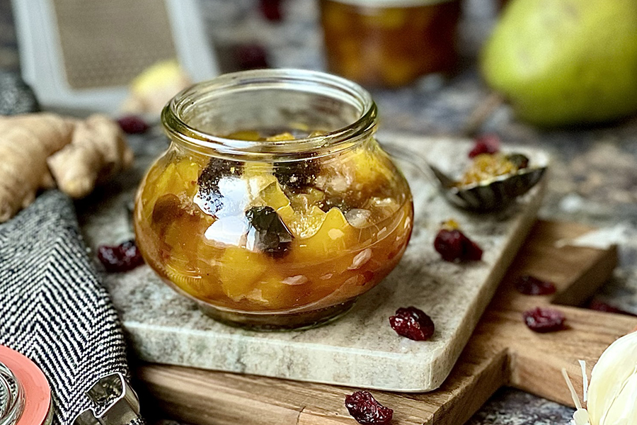 Birnen-Cranberry-Chutney Ein Glas mit selbstgemachtem Chutney, umgeben von Cranberries und Ingwer, auf einem Marmortablett
