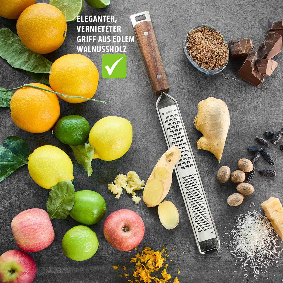 Reibe mit Walnussholzgriff, Zitrusfrüchte, Gewürze und Schokolade auf grauem Tisch