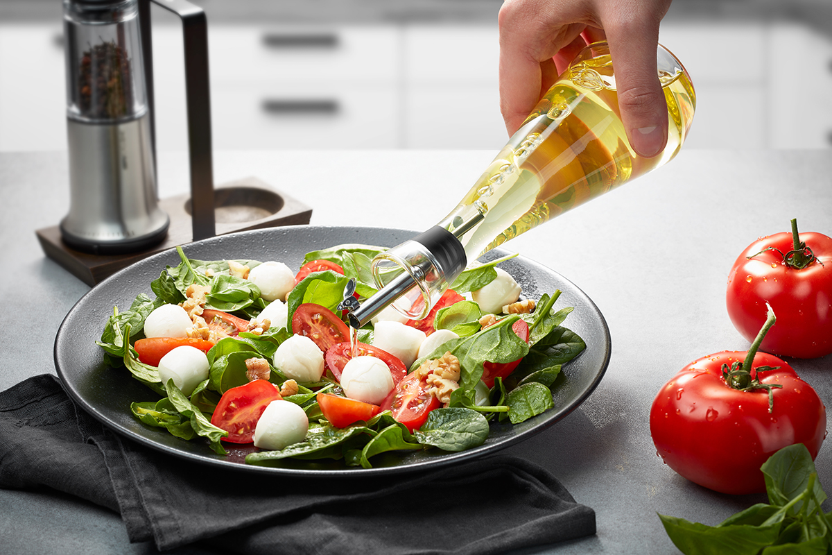 Leckerer frischer Spinatsalat mit Tomaten, Mozzarella und Walnüssen, serviert mit hochwertigem Olivenöl Hand gießt Olivenöl über einen frischen Spinatsalat mit Mozzarella, Tomaten und Walnüssen