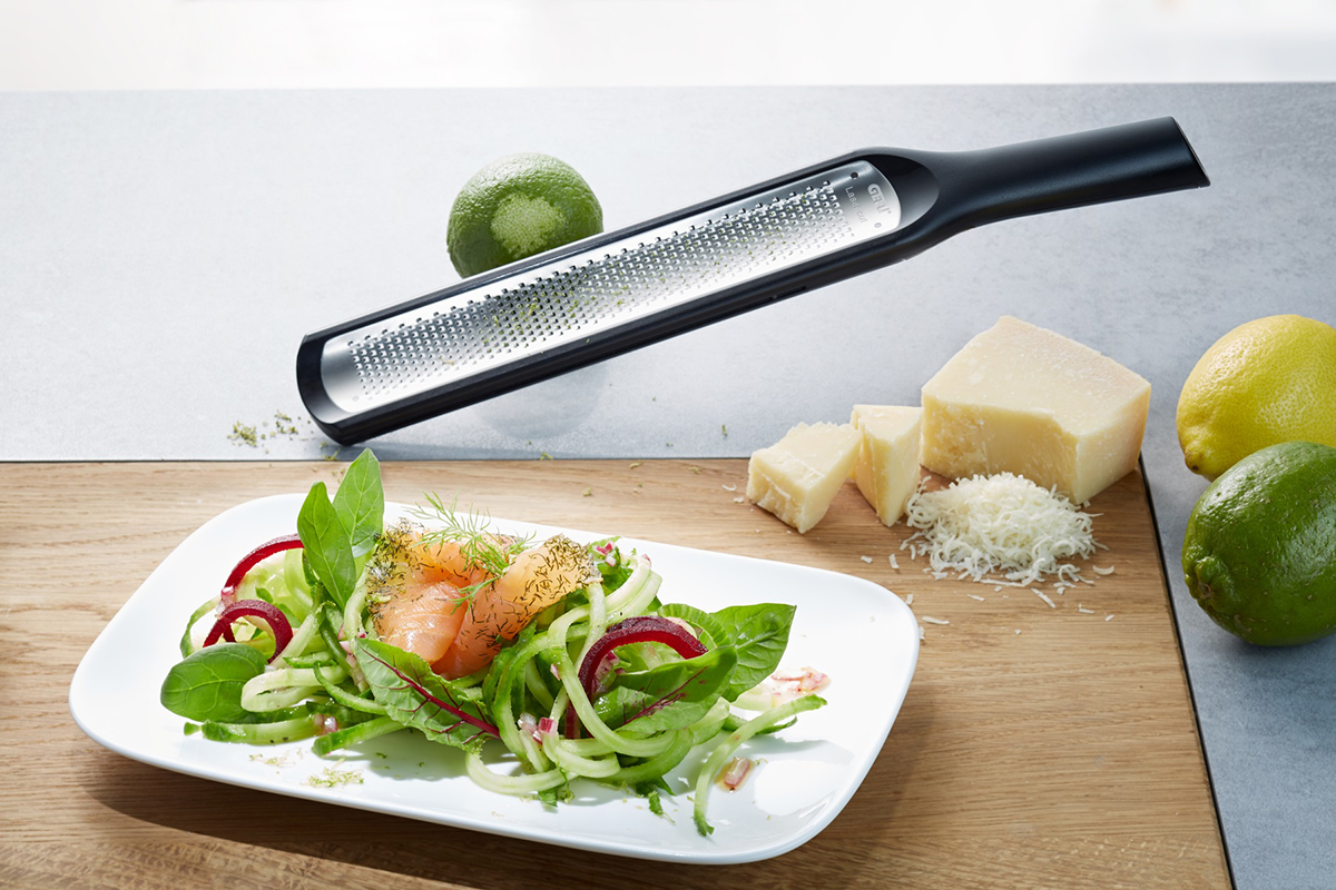 Gemüsereibe neben einem Teller mit Salat und geriebenem Käse auf einem Schneidebrett