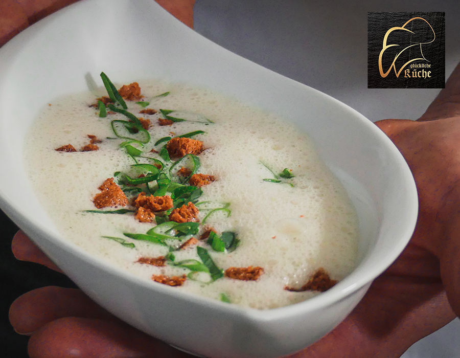 Kartoffelcremesüppchen Eine schaumige Suppe in einer weißen Schale, dekoriert mit frischen Kräutern und knusprigen Croûtons.