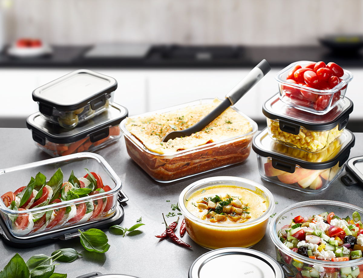 Vorratsdosen-Set aus Glas für frische Lebensmittelaufbewahrung Verschiedene Glasvorratsbehälter mit Deckeln, gefüllt mit Lasagne, Salat und Gemüse, auf einer Küchenarbeitsplatte