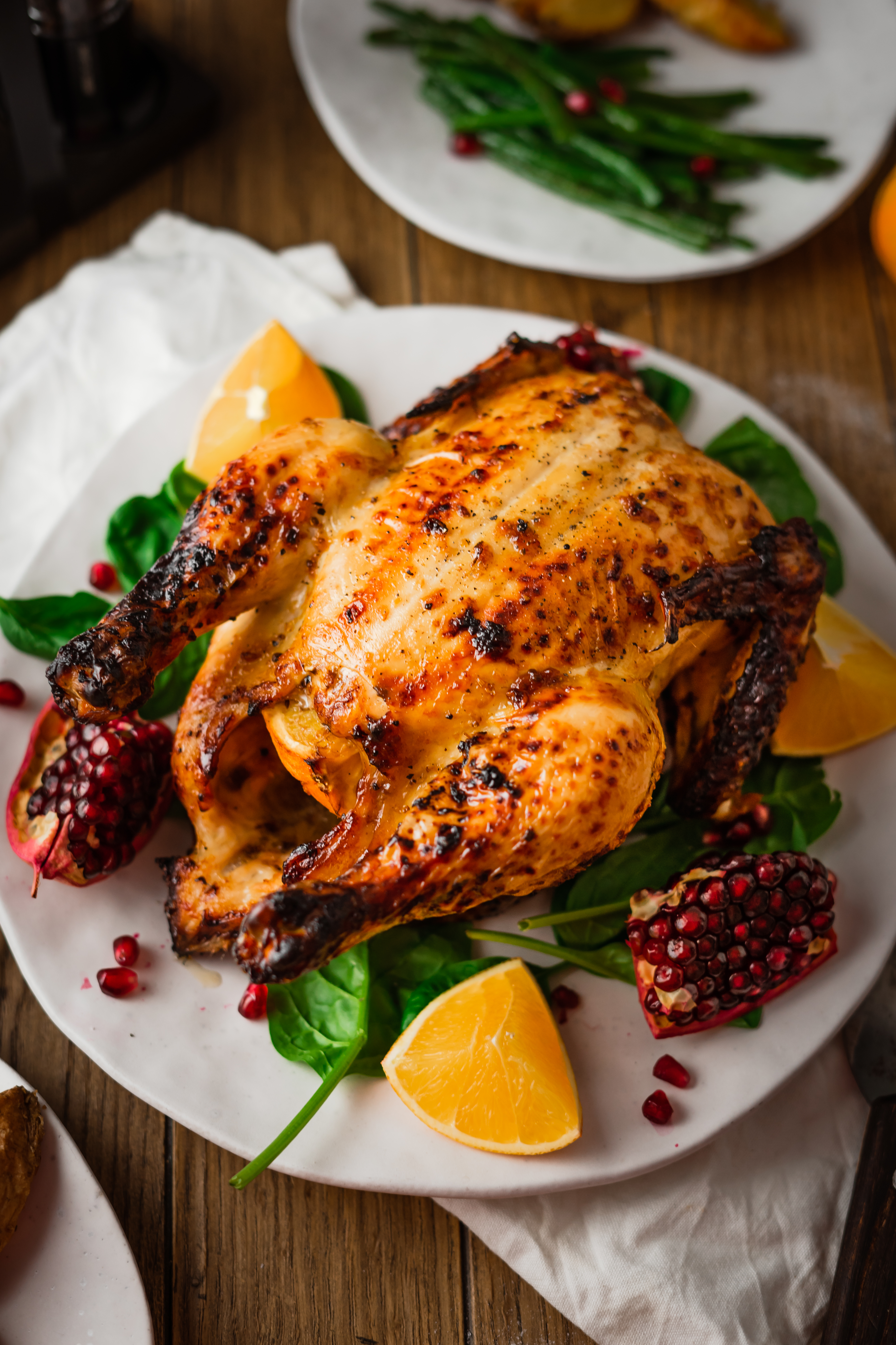 Orangenhähnchen fürs Weihnachtsessen Ein gebratenes Hähnchen serviert mit Orangenscheiben und Granatapfel auf einem Teller, dekoriert mit grünem Spinat.